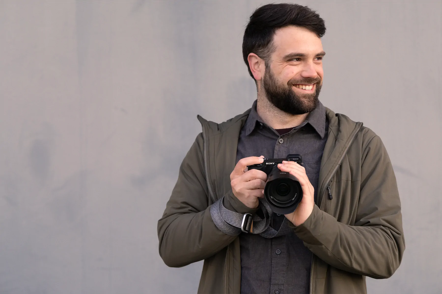 Portrait of Ryan Moelter smiling and holding a camera against a textured gray background